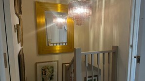 Ein Flur mit einer Chandelüster, einem Spiegel und gerahmten Kunstwerken an den Wänden.