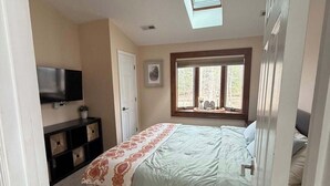Un dormitorio con cama, ventilador de techo, televisión, ventana y puerta.