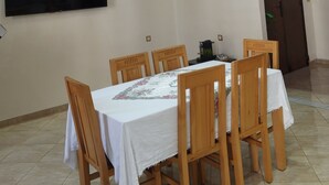 Un comedor con una mesa grande, sillas de madera, un televisor de pantalla plana en la pared, luces empotradas en el techo y una puerta al fondo.