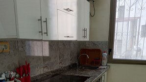 Una cocina con armarios blancos, encimera de granito, lavadora y ventana con rejas.