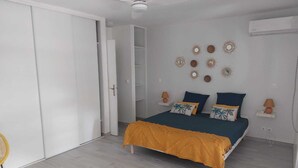 Un dormitorio con cama, ventilador de techo, armario y una pequeña mesa con silla.