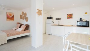 Apartamento moderno y funcional con kitchenette, zona de comedor y cama con ropa de cama estampada.