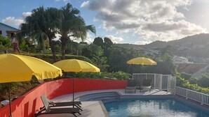 Una piscina con sombrillas amarillas, asientos rojos y vistas a colinas al fondo.