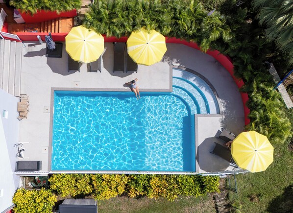 Vista aérea de una piscina rodeada de tumbonas y sombrillas, en un entorno de vegetación.
