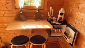 Een compact houten hutje met een kitchenette, inclusief een koelkast, een tafel en twee krukjes.