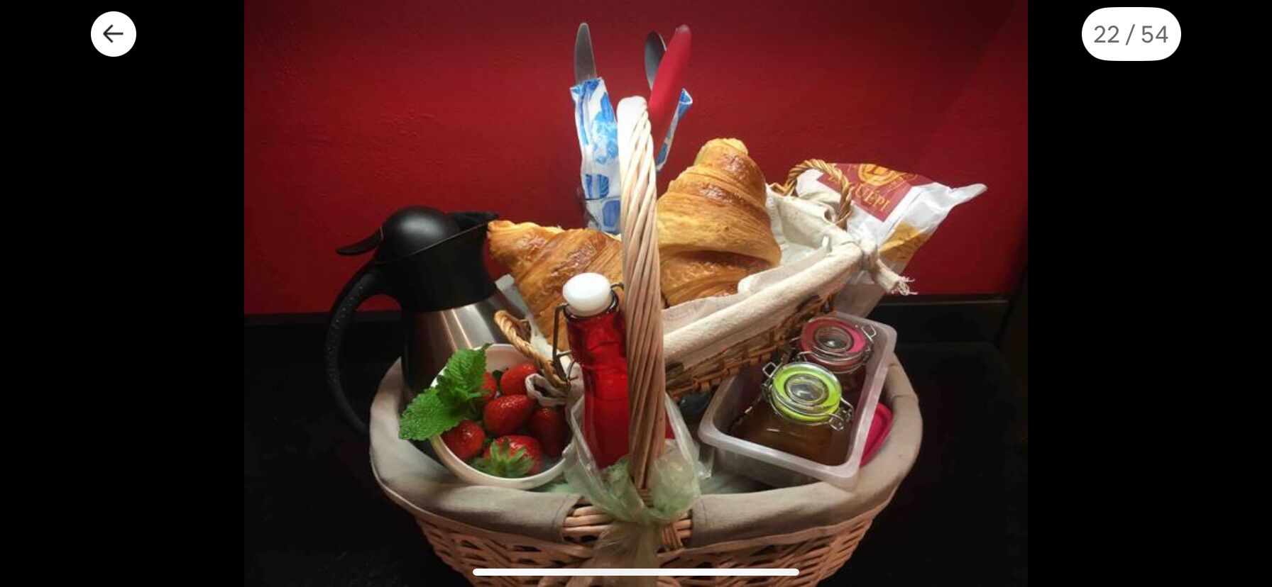 A basket containing croissants, strawberries, a red bottle, and a thermos.