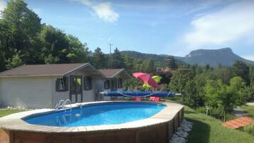 A swimming pool with a wooden deck, a slide, and a view of a mountain.