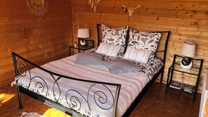 Een slaapkamer in een houten hutje, met een bed, twee nachtkastjes, een hanglamp en een welkomstbord.
