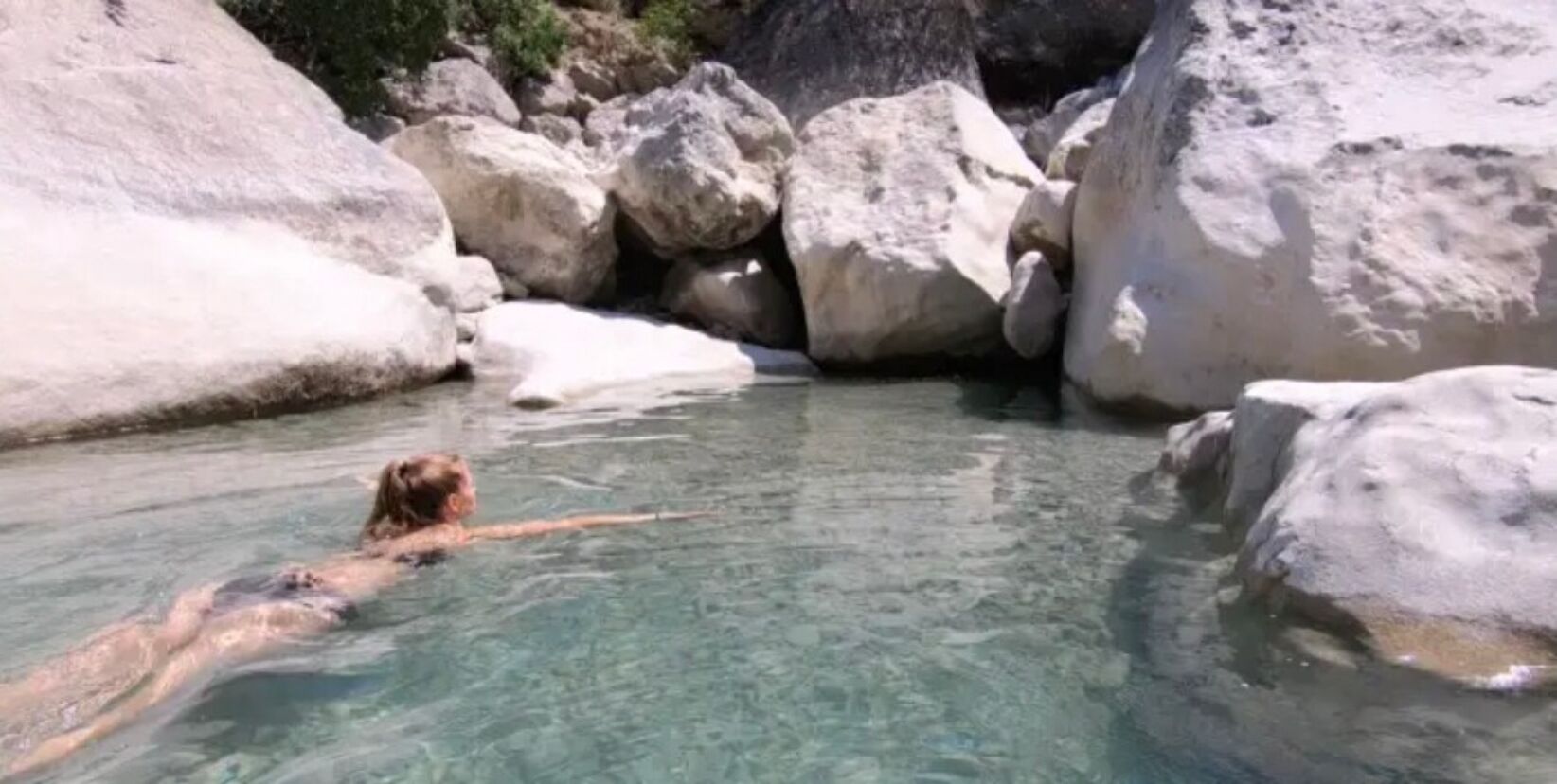 A person swimming in a natural pool surrounded by large rocks.
