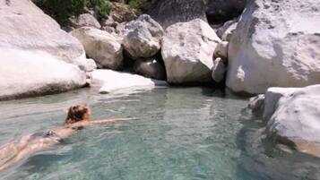 A person swimming in a natural pool surrounded by large rocks.