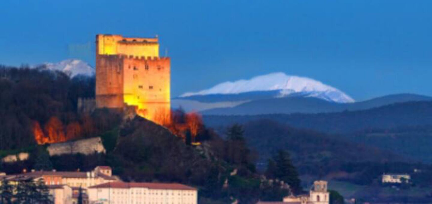 Un castillo con una torre, rodeado de árboles y una montaña al fondo.