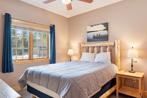 Une chambre à coucher avec un lit, deux tables de chevet avec des lampes, une fenêtre avec des rideaux et un tableau au mur.