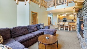 A spacious living room with a large sectional sofa, a round coffee table, and a stone fireplace.