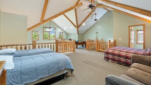 A spacious loft bedroom with two beds, a pool table, and a ceiling fan.