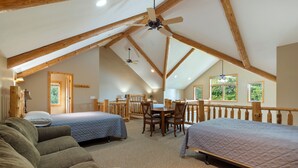 A spacious attic bedroom with two beds, a wooden ceiling, and a balcony.