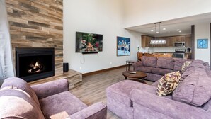 A modern living room with a fireplace, purple sofas, and a kitchen in the background. - Luxury Townhome|Heart of Crosslake|Beach 832 (Crosslake)