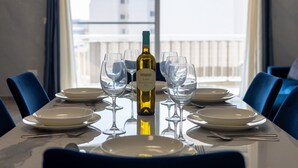 A dining table set with plates, glasses, and a bottle of wine, with a view of buildings through a window. - Beautifully Furnished 3 Bedroom Home in Qawra (Saint Paul's Bay)