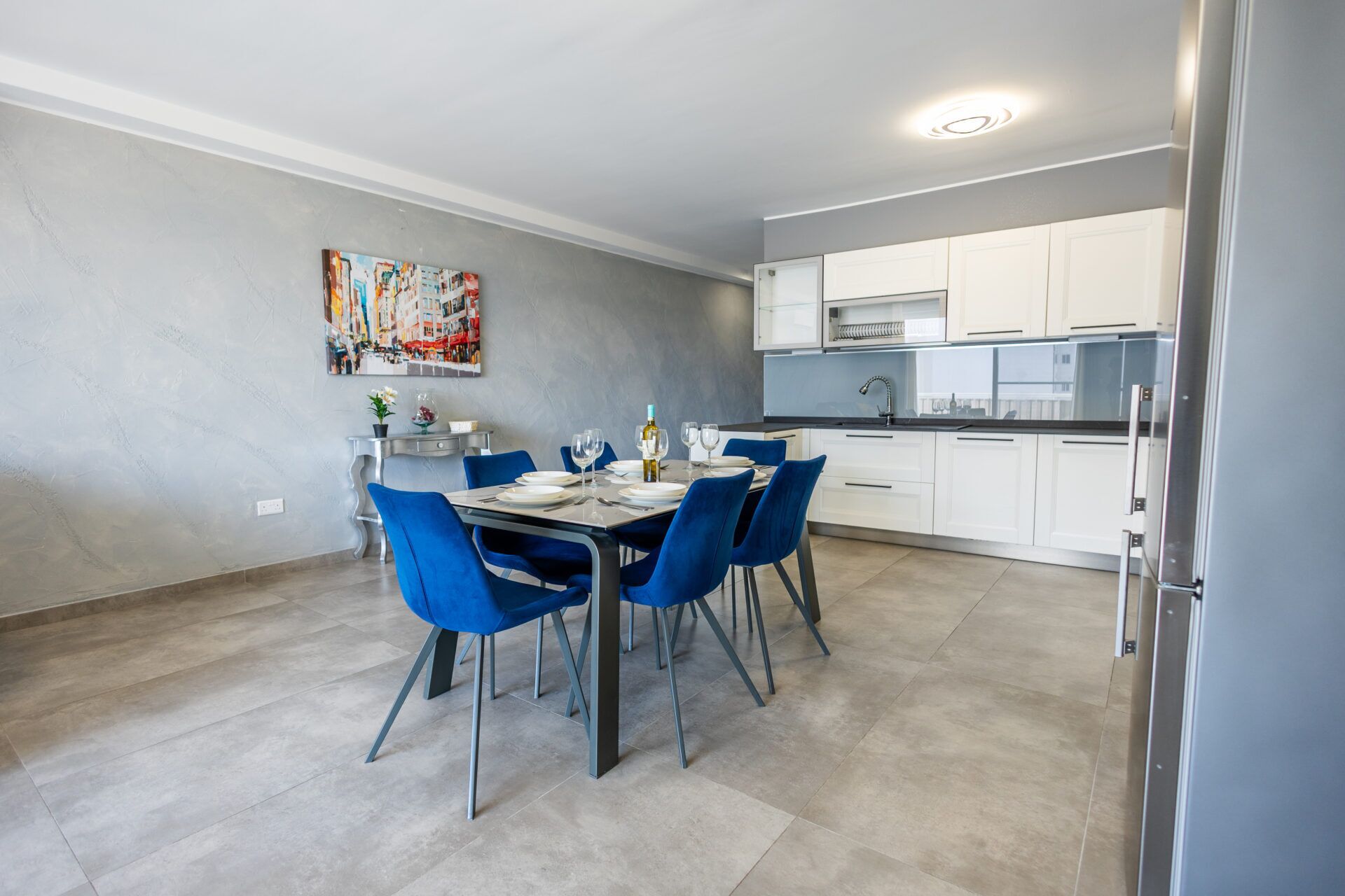A modern kitchen with white cabinets and a dining area with blue chairs.