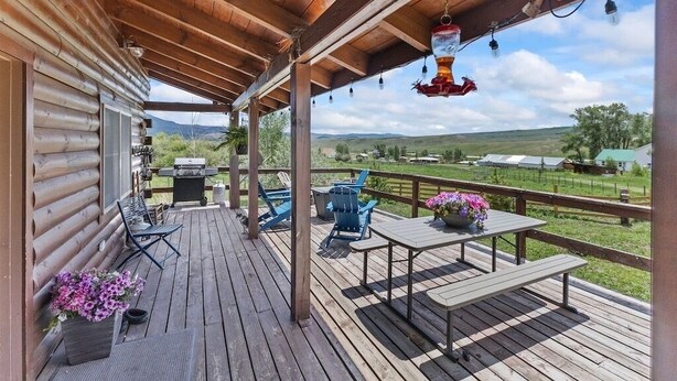 A wooden deck with outdoor furniture, a barbecue grill, and a scenic view of the countryside.