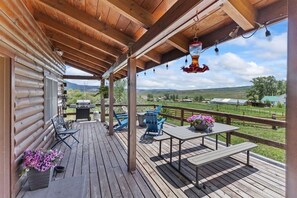 A wooden deck with outdoor furniture, a barbecue grill, and a scenic view of the countryside.