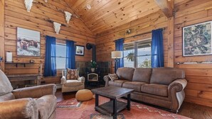 A rustic cabin interior with wooden walls, a leather sofa, a coffee table, and a fireplace.