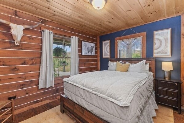 A wooden cabin bedroom with a bed, curtains, a nightstand, and a cow skull decoration.