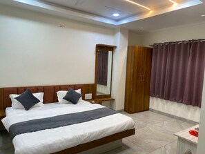 A modern bedroom with a large bed, a wooden wardrobe, a mirror, and purple curtains. - Hotel Shree Nakoda Paradise (Ujjain)