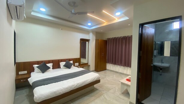 Une chambre d’hôtel moderne dotée d’un grand lit, d’un ventilateur de plafond, d’un éclairage encastré, d’un miroir, d’une armoire et d’une salle de bain avec un lavabo et une douche.