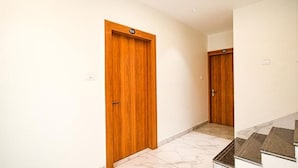 Un couloir avec des portes en bois, un sol en marbre et un escalier recouvert de carreaux foncés.