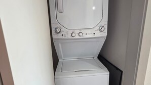 Une petite buanderie blanche, équipée d’un lave-linge et d’un sèche-linge à chargement frontal, dotée de boutons de commande et d’une petite fenêtre sur le sèche-linge.