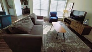 Un salon avec un canapé, une table basse, un téléviseur et, au fond, un coin cuisine.