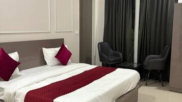 A hotel room with a large bed, two chairs, an air conditioning unit, and a door.