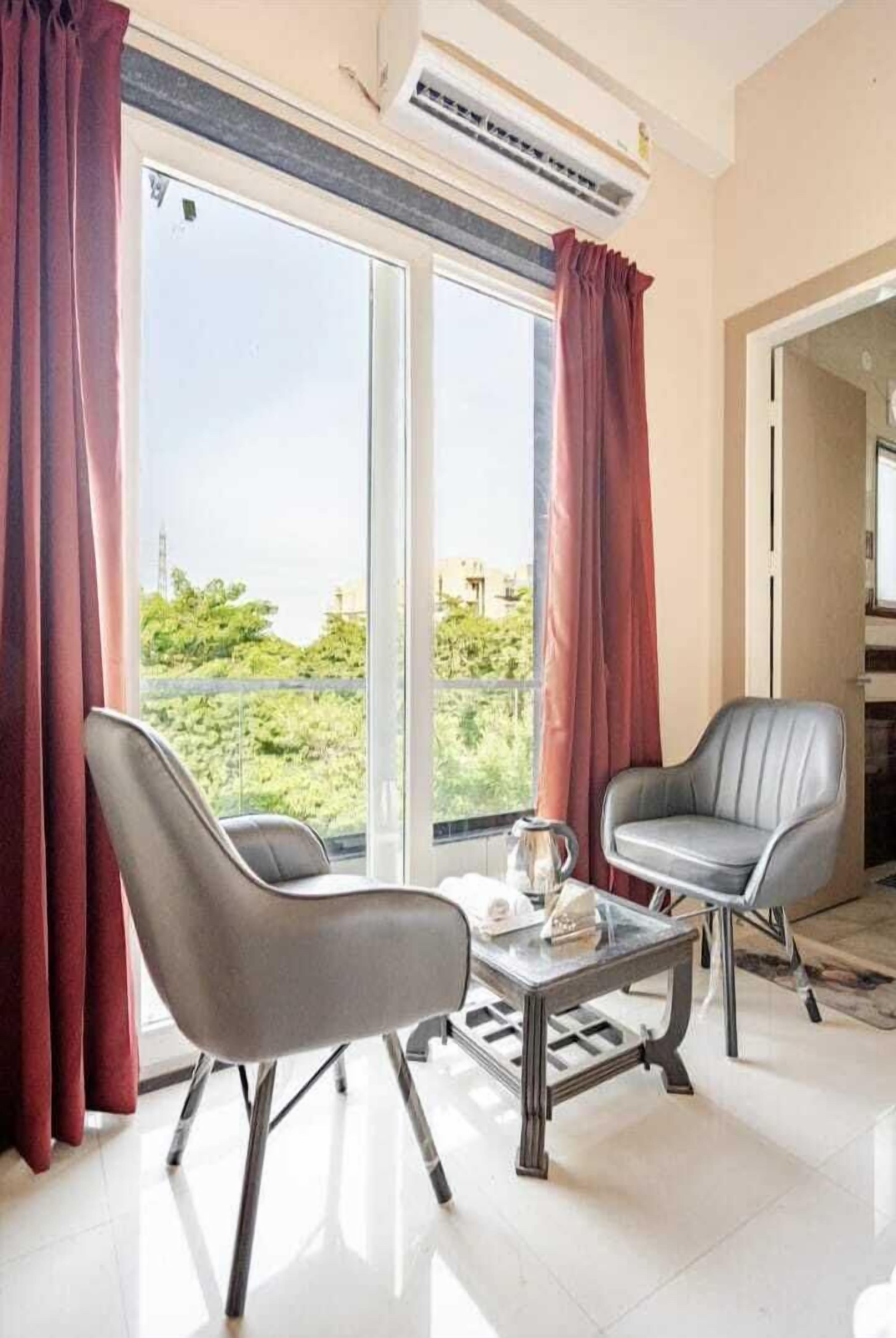 A modern living room with two leather chairs, a coffee table, and a large window with curtains.