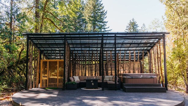 A circular wooden deck with a covered seating area, a hot tub, and a glass door entrance.