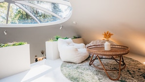 A modern interior with a round table, white poufs, and a large window with a view of trees.