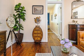 A room with a wooden floor, a tripod-mounted clock, a potted plant, a wooden cabinet, and a vase with flowers. - Luxury 3BR/3BA•Air Hockey Lounge•Walkable Old City (Philadelphia)
