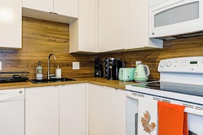 Eine moderne Küche mit weißen Schränken, einer Holz-Spritzschutzleiste, einer Mikrowelle, einer Kaffeemaschine, einem Toaster und einem Geschirrspüler.