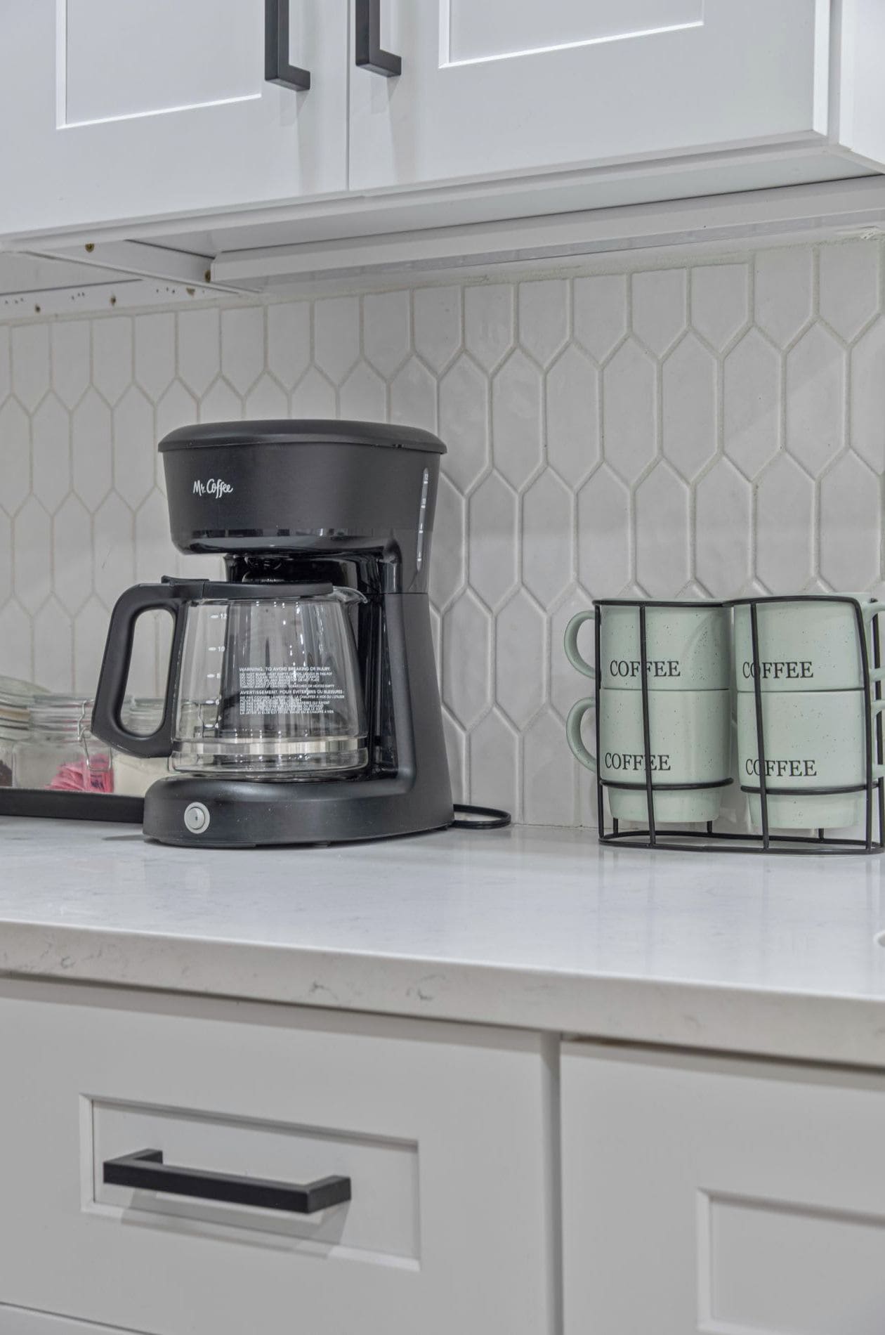 A kitchen with a coffee maker, a glass carafe, and two coffee containers on the counter.