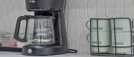 A kitchen with a coffee maker, a glass carafe, and two coffee containers on the counter.