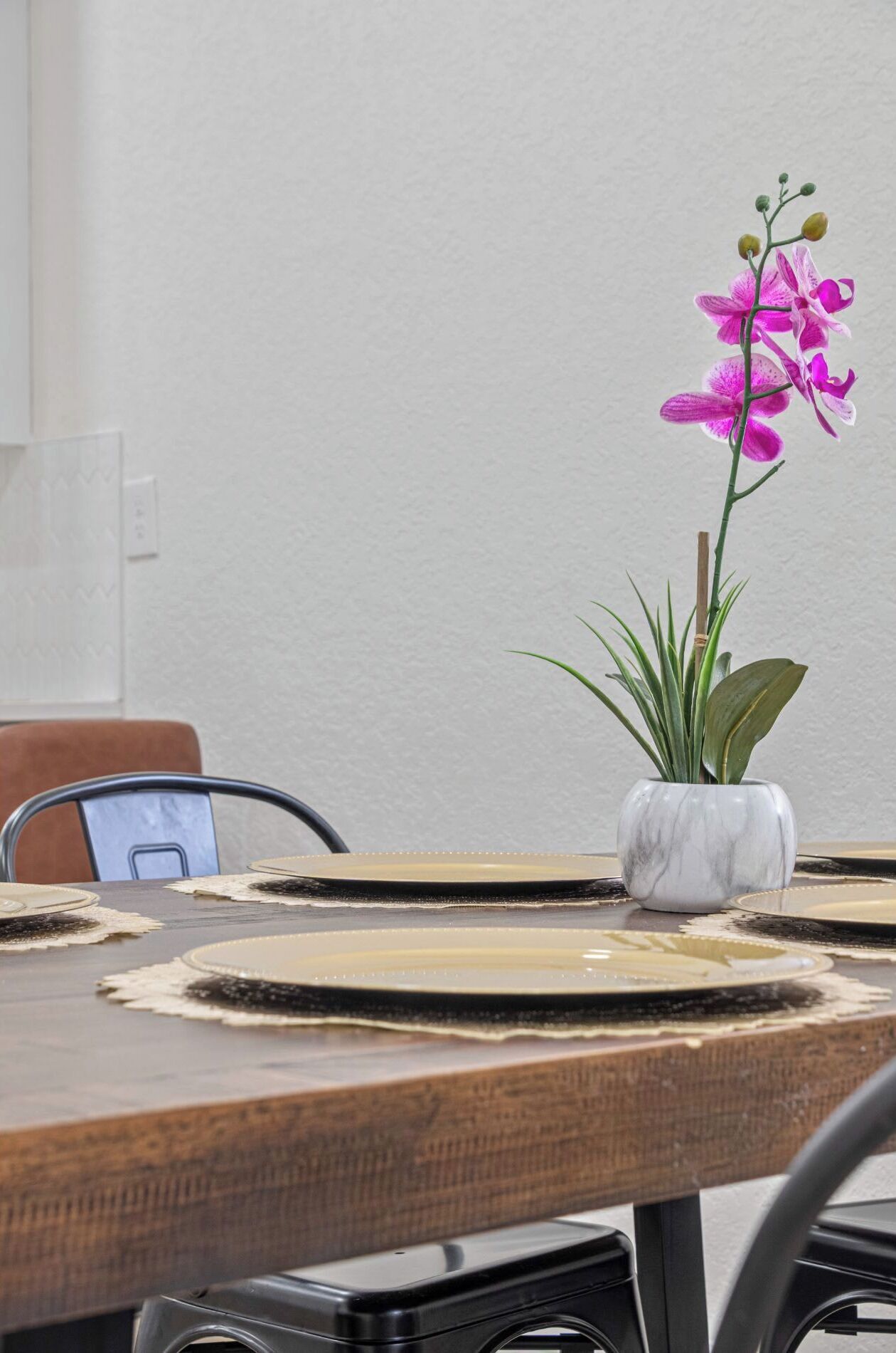A dining table with a white vase containing a pink orchid and a green plant.