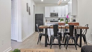Una cocina moderna con armarios blancos, una isla central y un comedor con mesa y sillas de madera.