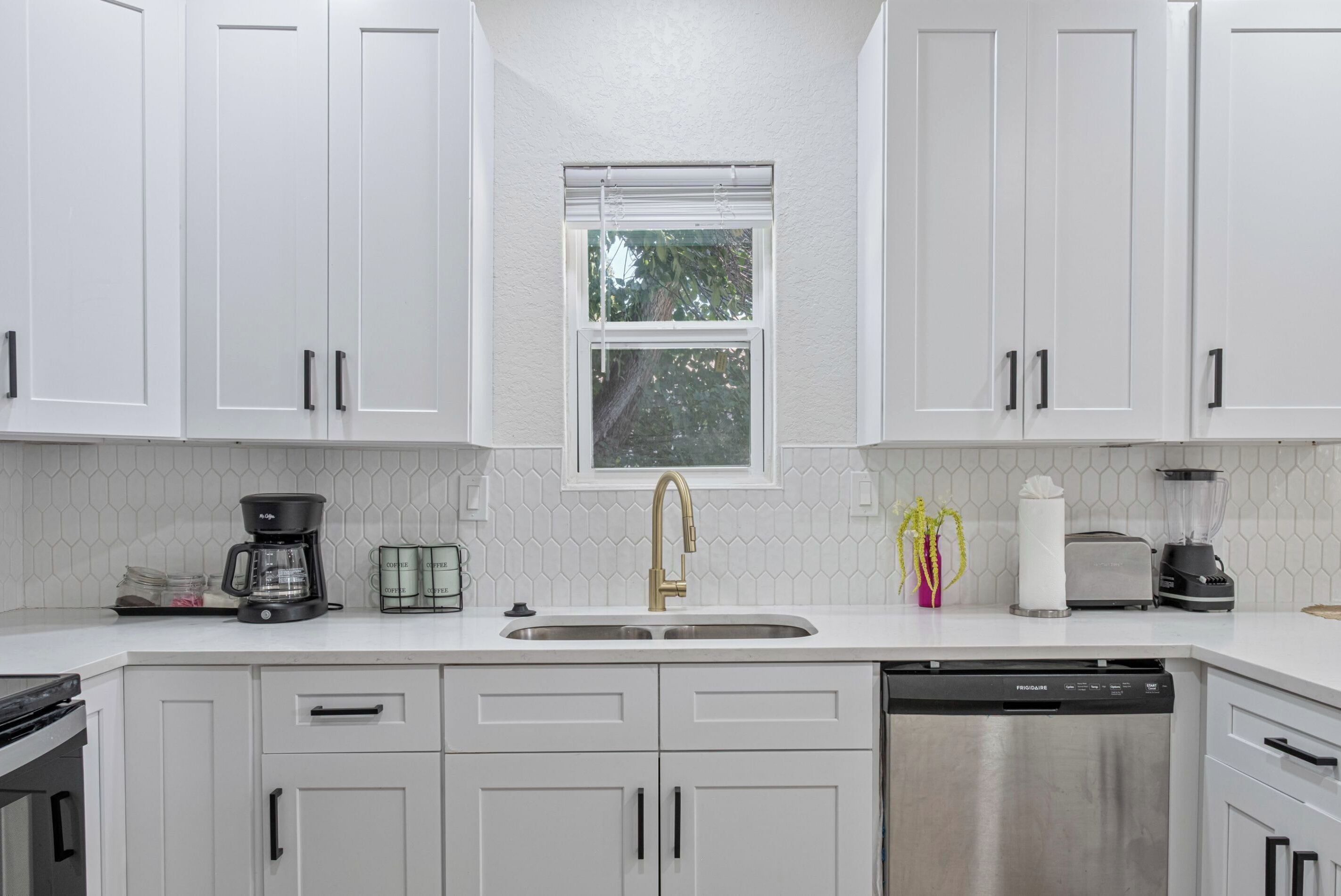 A modern kitchen with white cabinets, a stainless steel dishwasher, a coffee maker, and a toaster.