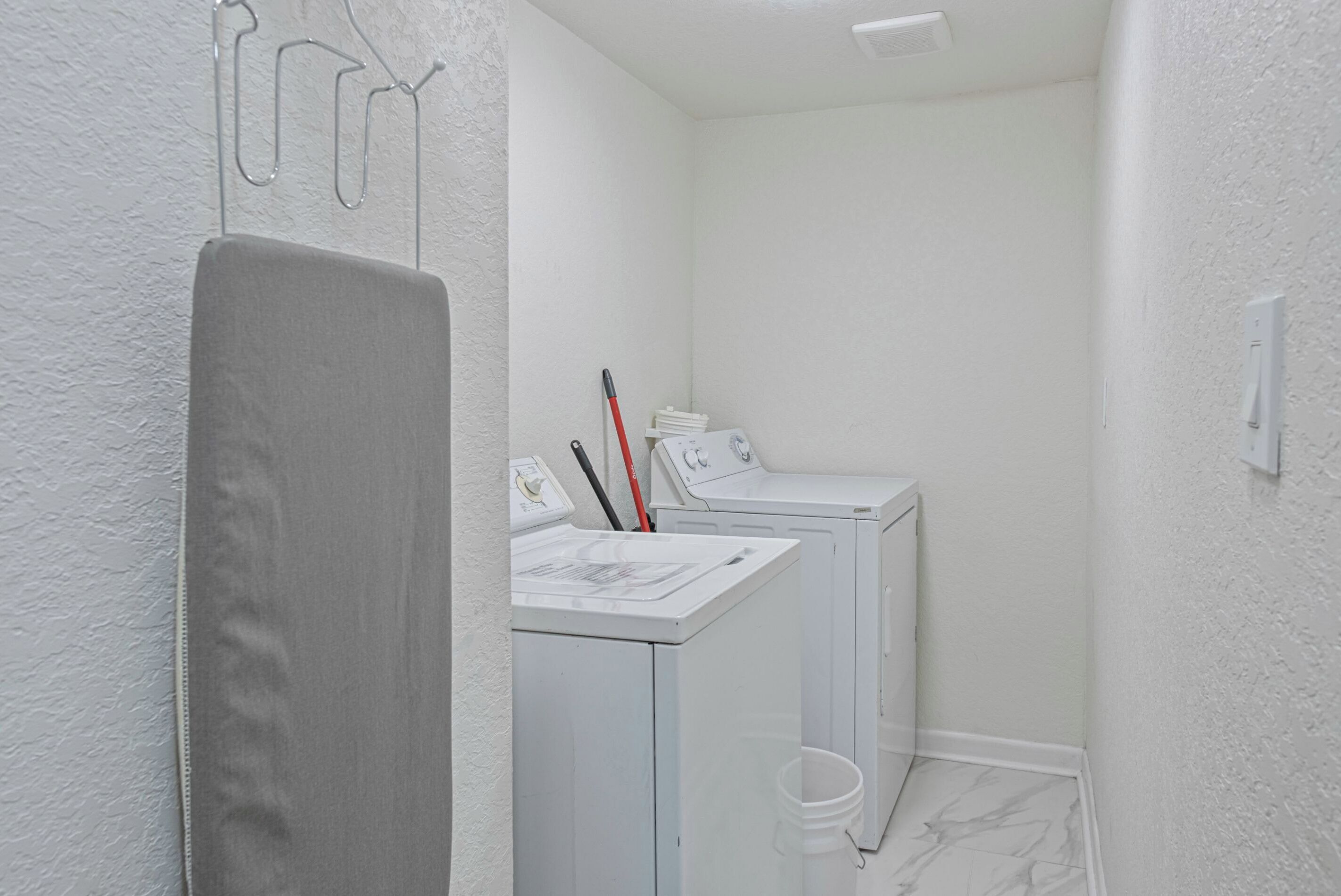 A laundry room with two washing machines, a drying rack, and a mop.