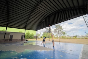 An outdoor basketball court with a metal roof, a basketball hoop, and a net.