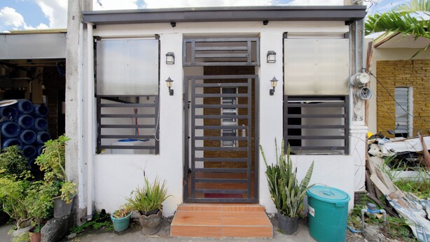 A building with a white exterior, a metal gate, and potted plants. - 1 Bedroom Lumina Home Subdivision in Bacolod City (Bacolod)