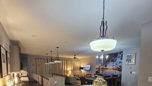 A modern kitchen with a central island, a dining area with a round table, and a living room with a TV. - Cruisehaus ATL- handicap accessible, 4 beds on main floor (Atlanta)