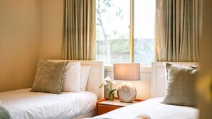 A hotel room with two beds, beige curtains, a bedside lamp, and a small table with a vase of flowers. - StayAU Family Retreat w/Pool Table in Cranbourne (Cranbourne)