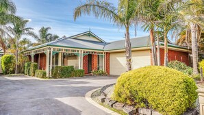 A two-story house with a covered porch, a garage, and a well-maintained garden with palm trees and shrubs. - StayAU Family Retreat w/Pool Table in Cranbourne (Cranbourne)