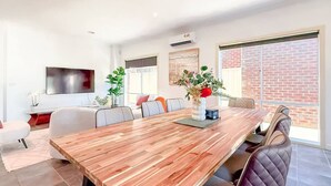A modern dining area with a wooden table, comfortable seating, a flat-screen TV, and a brick wall.