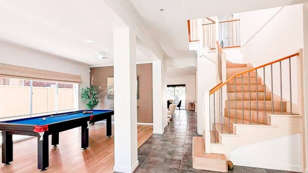 A spacious indoor area with a pool table, a staircase, and a view into another room.